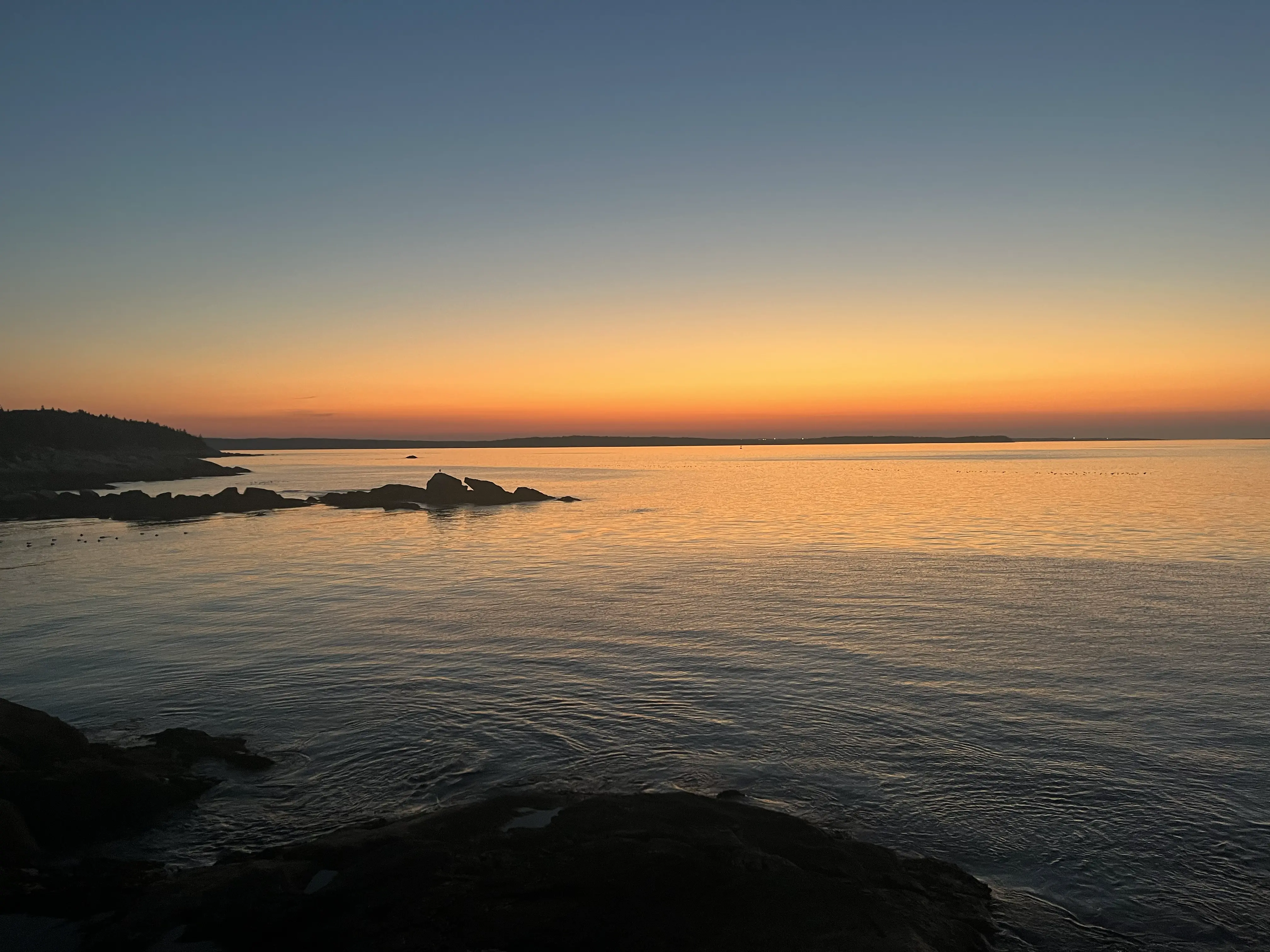 Sonnenaufgang über dem Atlantik in Nova Scotia, orange leuchtender Horizont über ruhigem Wasser, im Vordergrund dunkle Felsen